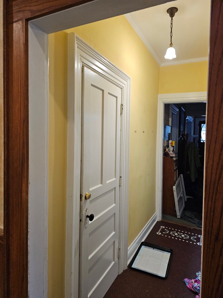 the same hall again, looking from the kitchen towards the yellow wall, with the white door about center