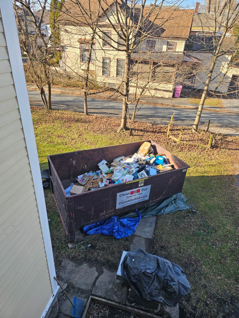 an overhead view of a large dumpster, about half full of trash. In the background you can see fall-bare trees and a beige house